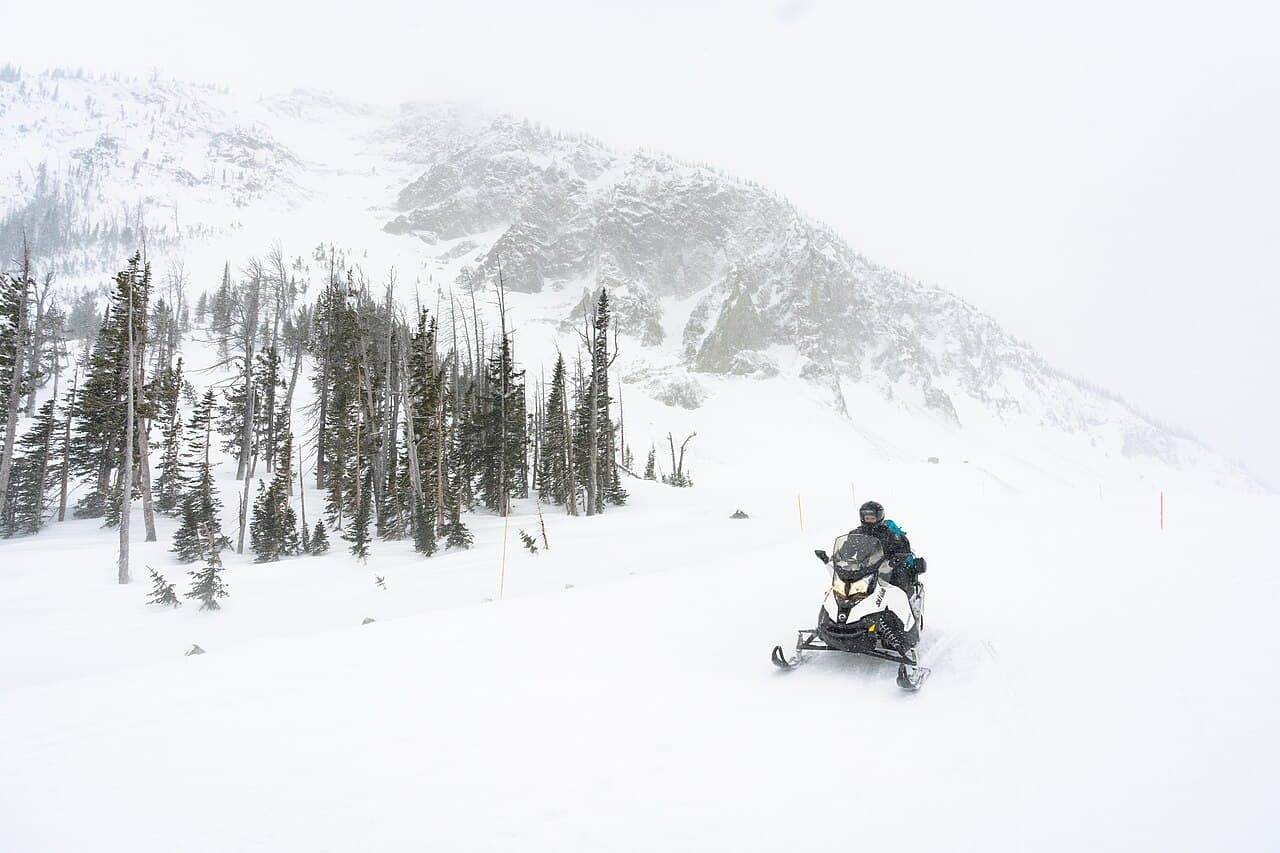 A single snowmobile rider crossing a mountain pass in falling snow